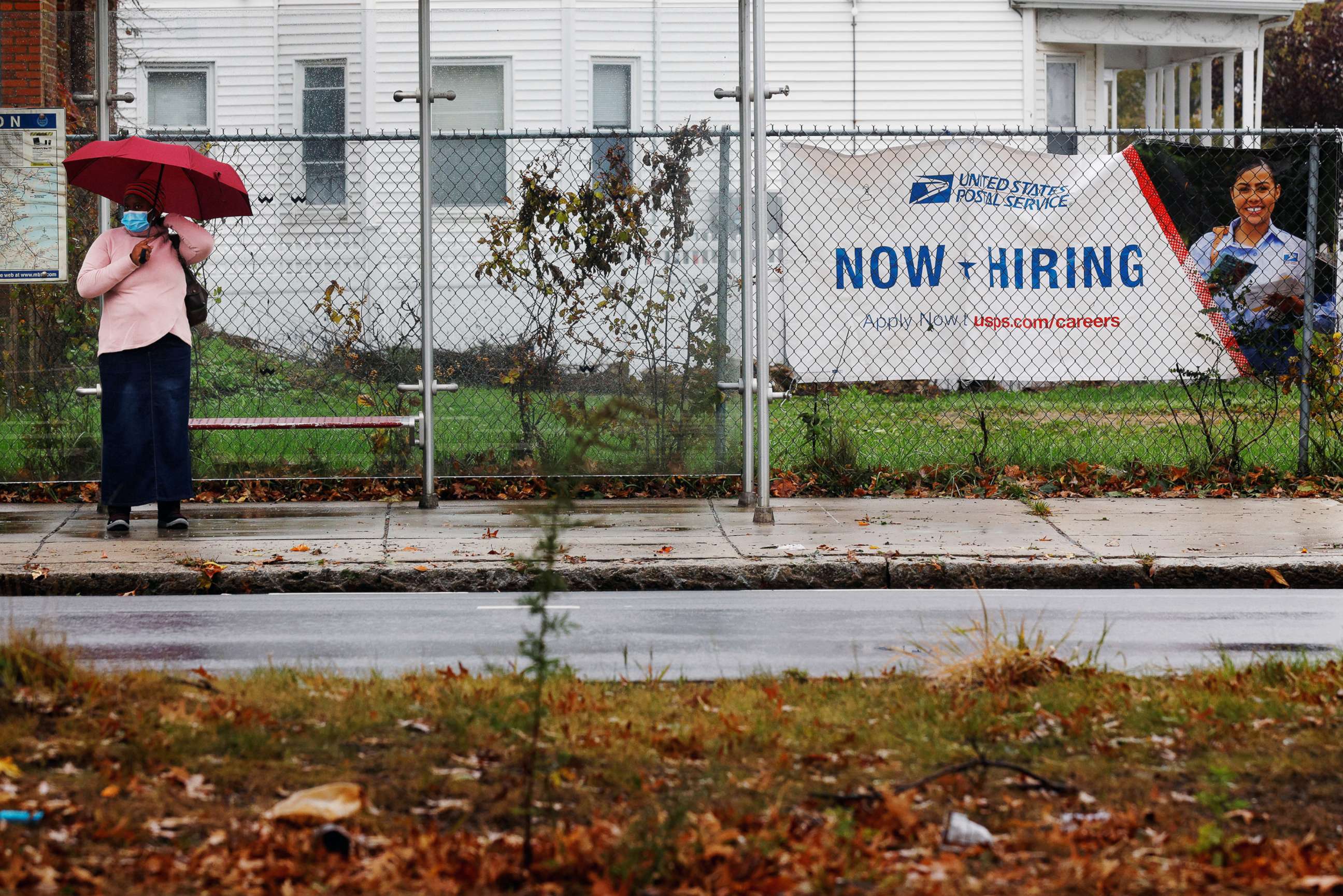 PHOTO: A woman waits for a bus next to a "Now Hiring" sign from the United States Postal Service in Boston, Oct. 30, 2021.