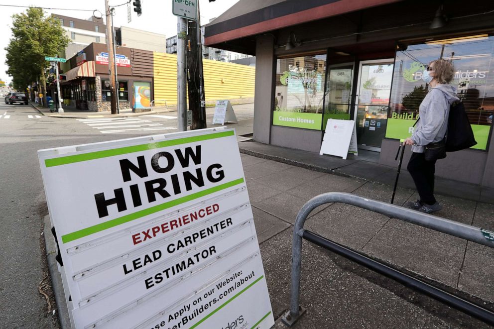 PHOTO: A pedestrian wearing a mask walks past reader board advertising a job opening for a remodeling company, in Seattle.