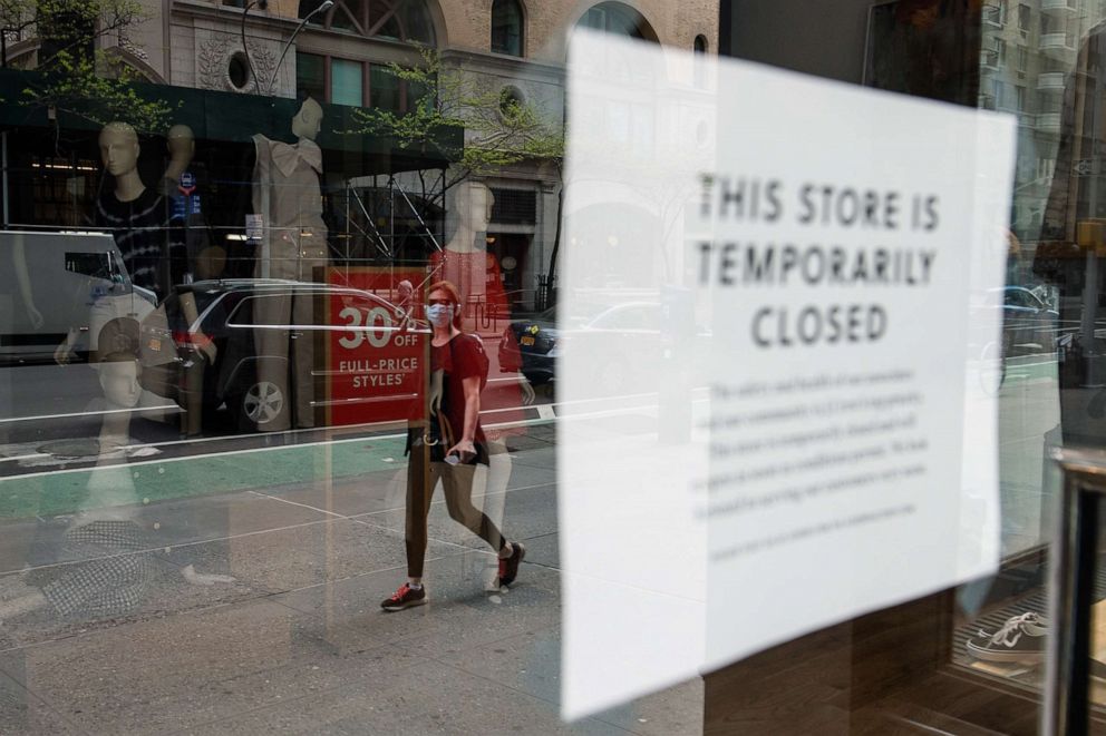 PHOTO: A woman wearing personal protective equipment walks past a closed J. Crew store on May 4, 2020 in New York.