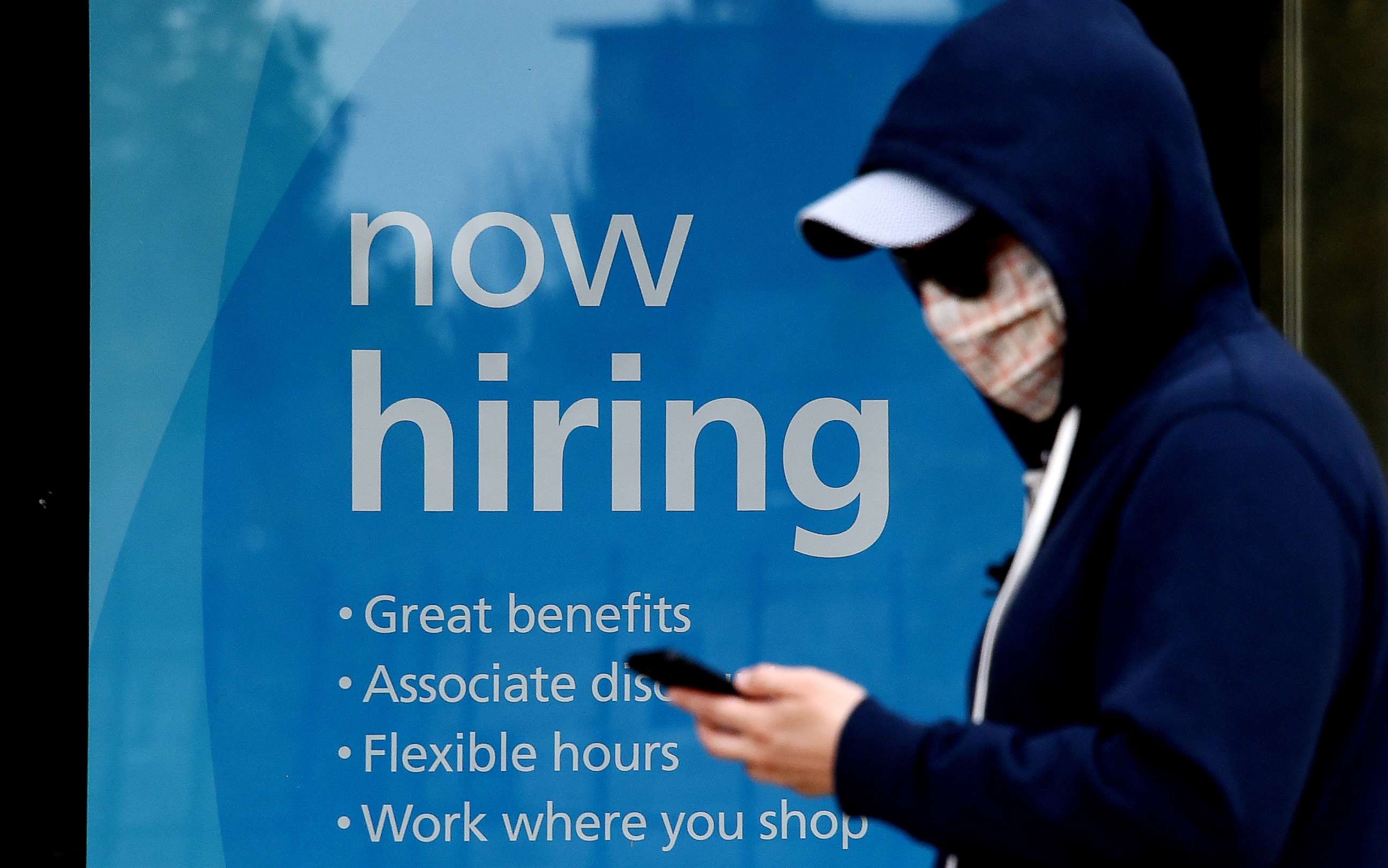 PHOTO: A man wearing a face mask walks past a sign "Now Hiring" in front of a store in Arlington, Va., May 14, 2020.