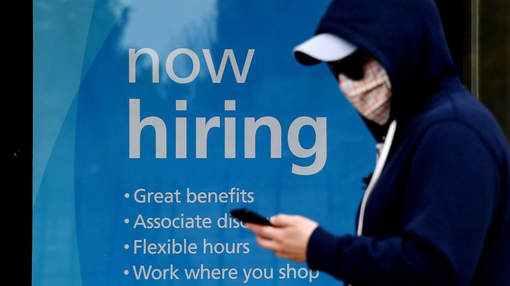 PHOTO: A man wearing a face mask walks past a sign "Now Hiring" in front of a store in Arlington, Va., May 14, 2020.