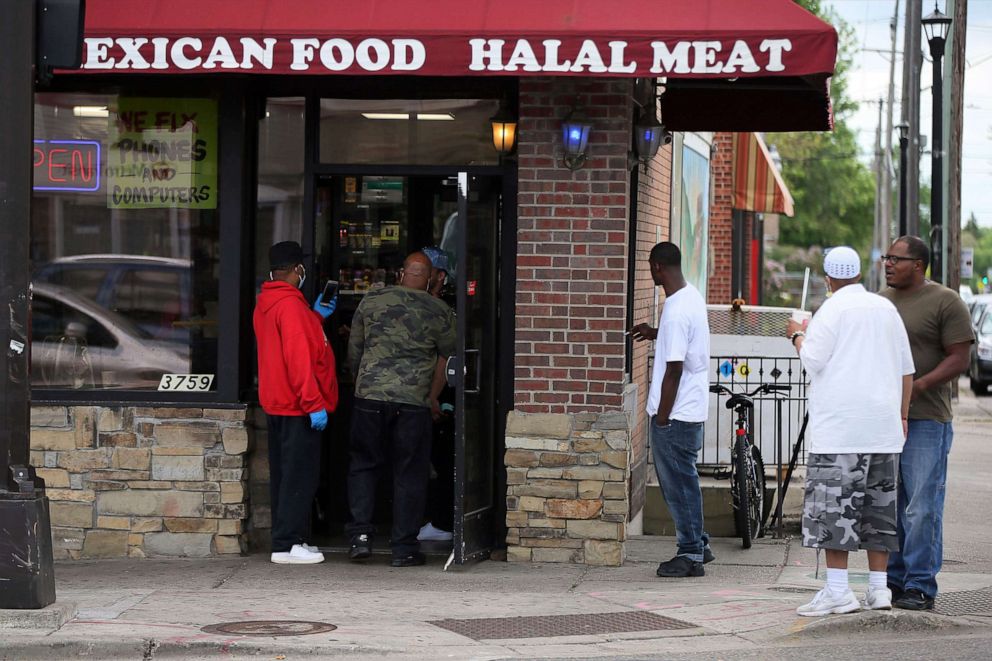 PHOTO: Men gather outside a grocery store Tuesday, May 26, 2020 near where a black man died in police custody Monday night in Minneapolis.