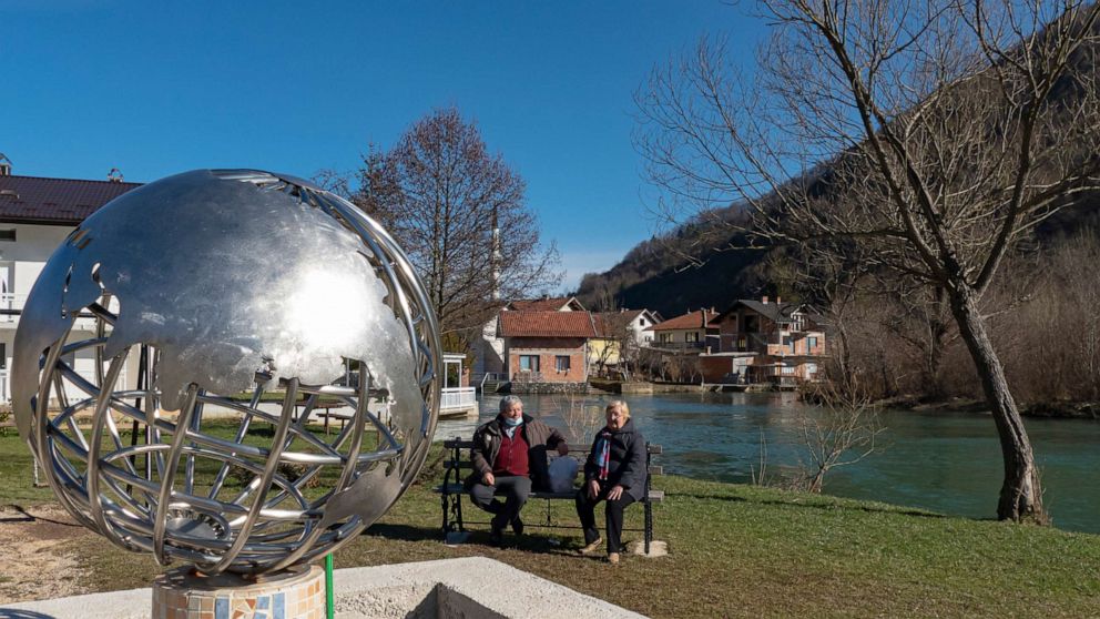 PHOTO: Residents sit near a metal representation of planet Earth in Jezero, Bosnia, Tuesday, Feb. 16, 2021.