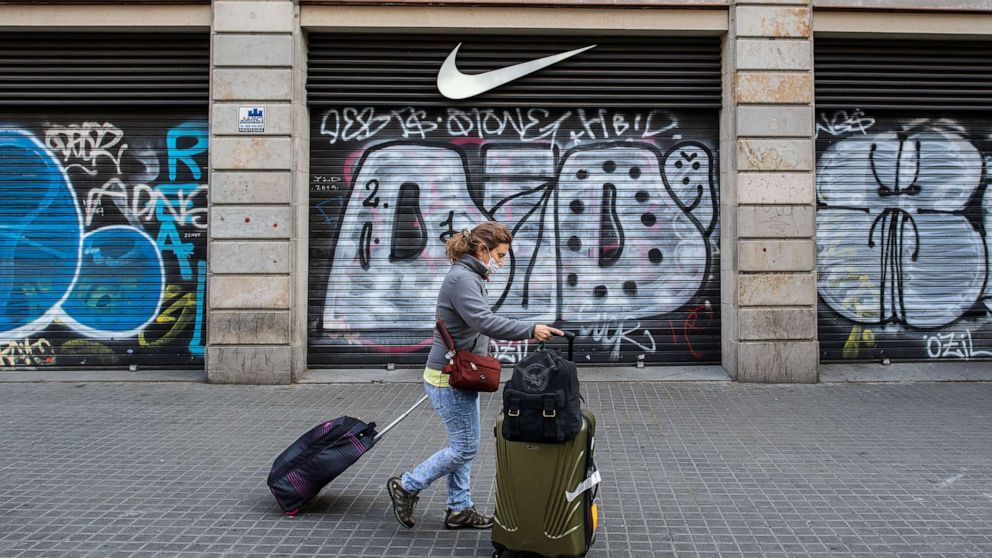 PHOTO: A tourist wears a protective mask as she carries her suitcases past a closed Nike store at Las Ramblas, March 15, 2020, in Barcelona, Spain. 