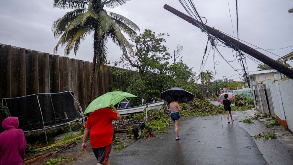 PHOTO: People walk on a street with power lines downed by the passing of Hurricane Fiona in Penuelas, Puerto Rico, Sept. 19, 2022.