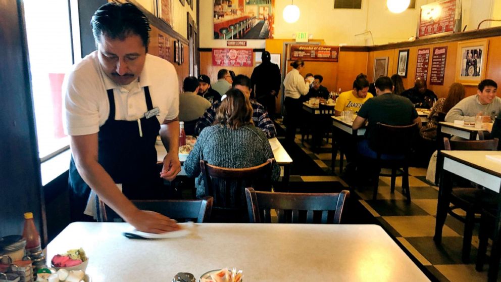 PHOTO: An unidentified employee at The Original Pantry Cafe in downtown Los Angeles wipes down a table, March 12, 2020.