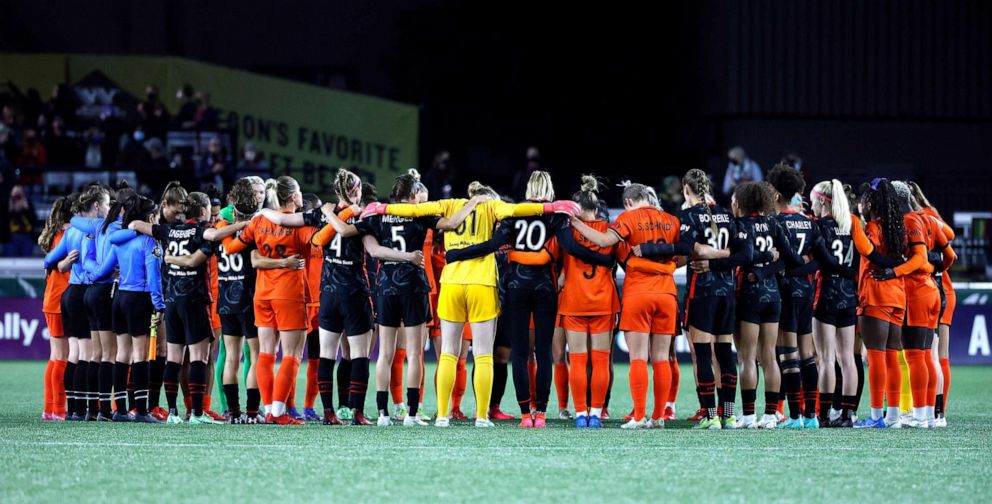 PHOTO: Portland Thorns and Houston Dash players stand together at the six minute mark during the first half of a NWSL soccer match at Providence Park in Portland, Oct 6, 2021.