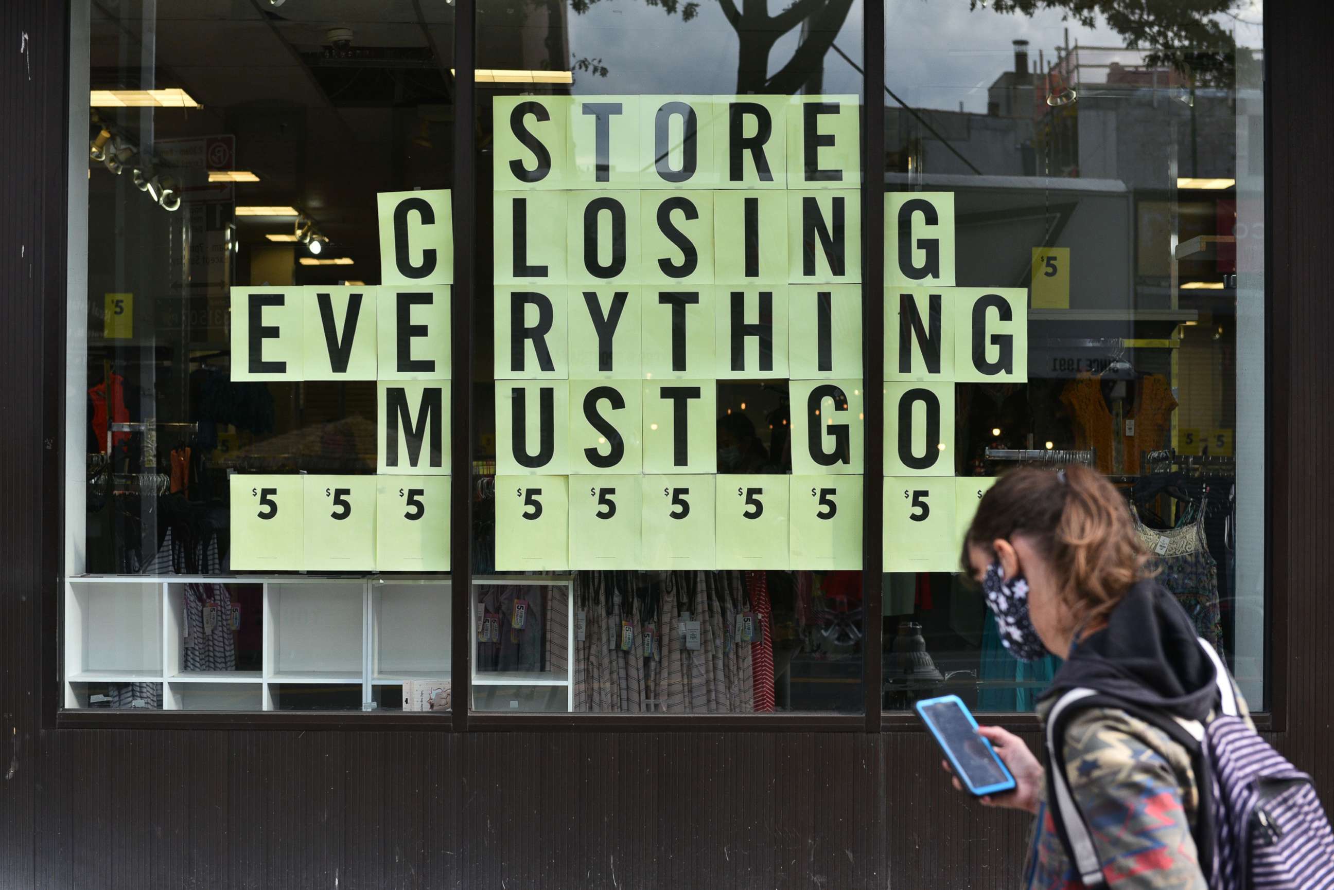 PHOTO: A woman checks her cell phone as she walks past a store closing sign in the Park Slope section of N.Y, Oct. 5, 2020.