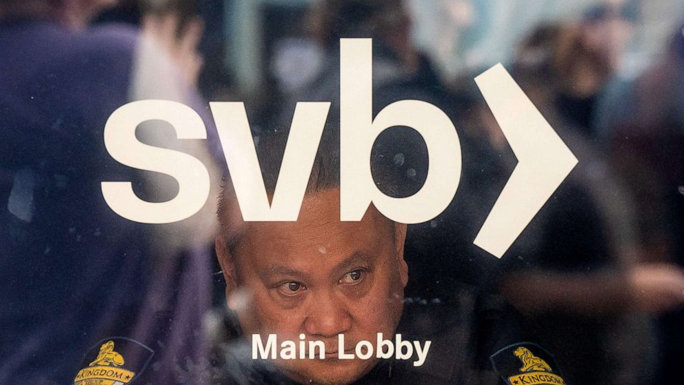 PHOTO: A security guard looks out a door as customers line up at Silicon Valley Bank headquarters in Santa Clara, Calif., Mar. 13, 2023.