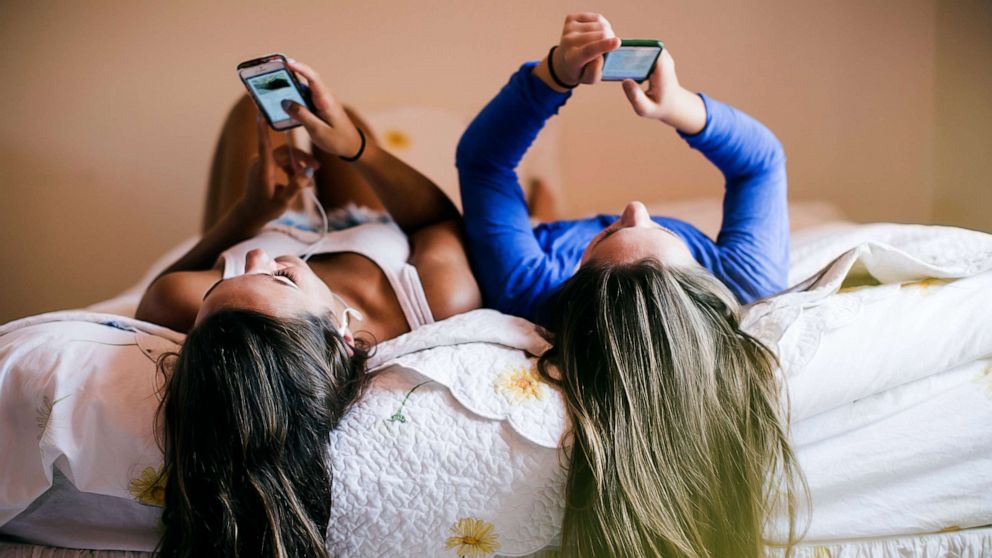 PHOTO: Teens use cellphones on a bed in this stock photo.