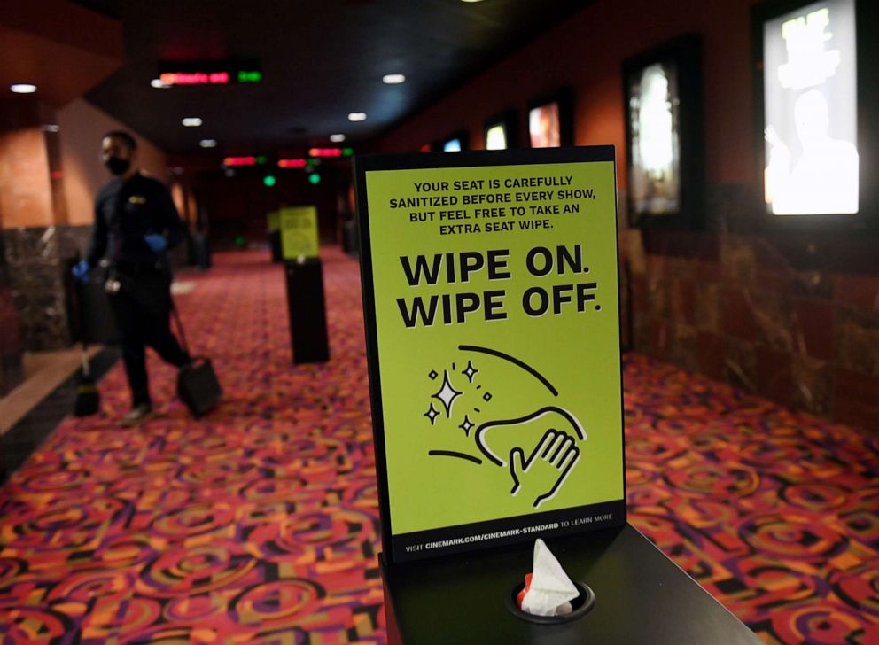 PHOTO: In this Aug. 14, 2020, file photo, an employee cleans a hallway as he walks by a seat wipe station at a theater in Las Vegas.