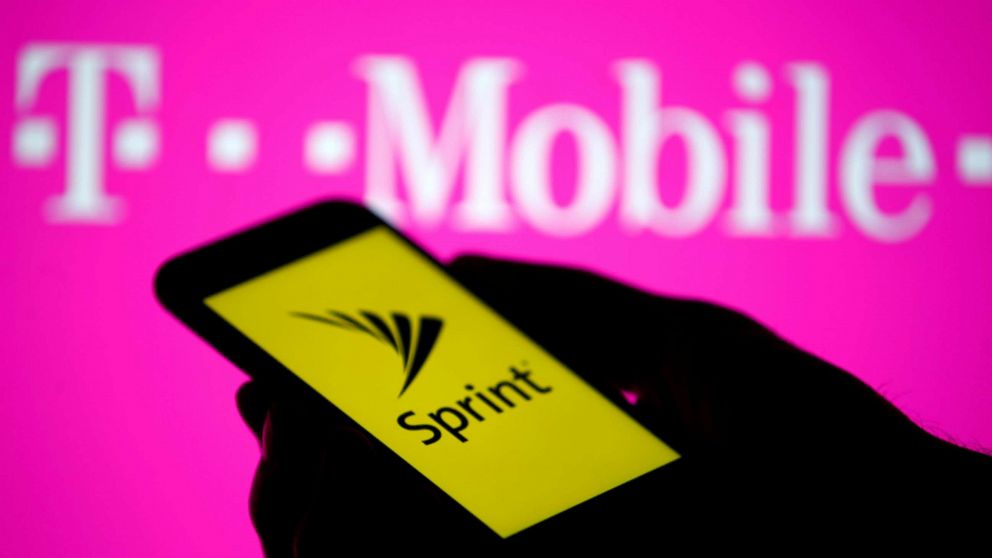 PHOTO: A posed photo shows a smartphone with Sprint logo in front of a screen projection of T-mobile logo.