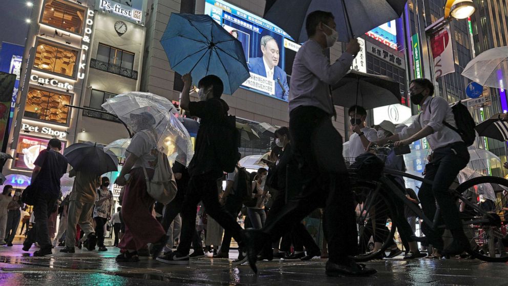 PHOTO: Pedestrians walk past at TV broadcasting a news conference by Japanese Prime Minister Yoshihide Suga after he announced a state of emergency because of rising coronavirus infections, July 8, 2021, in Tokyo.