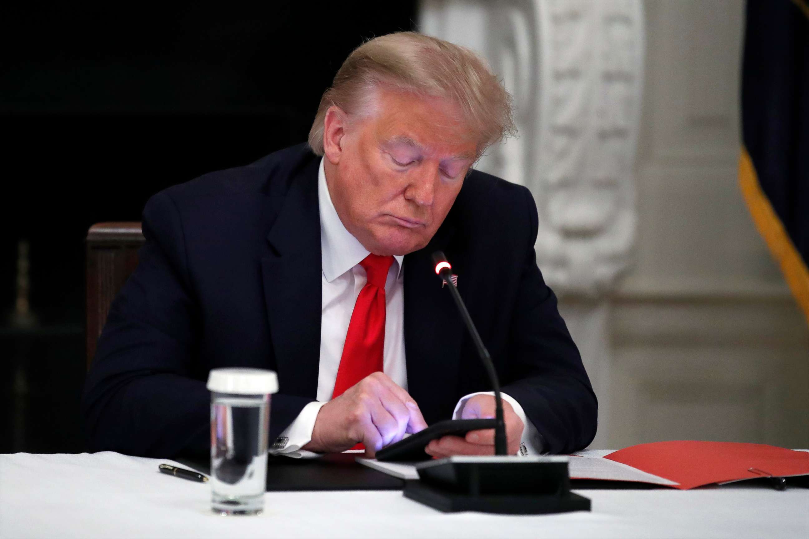 PHOTO: President Donald Trump looks at his phone during a roundtable with governors on the reopening of America's small businesses, in the State Dining Room of the White House in Washington.