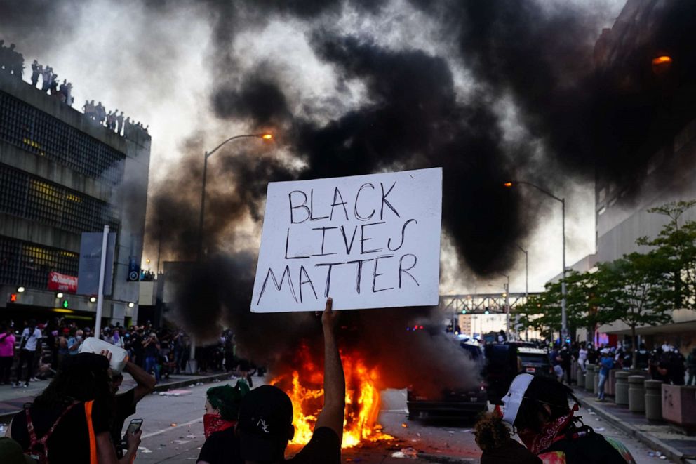 PHOTO: A man holds a Black Lives Matter sign as a police car burns during a protest in Atlanta, May 29, 2020.