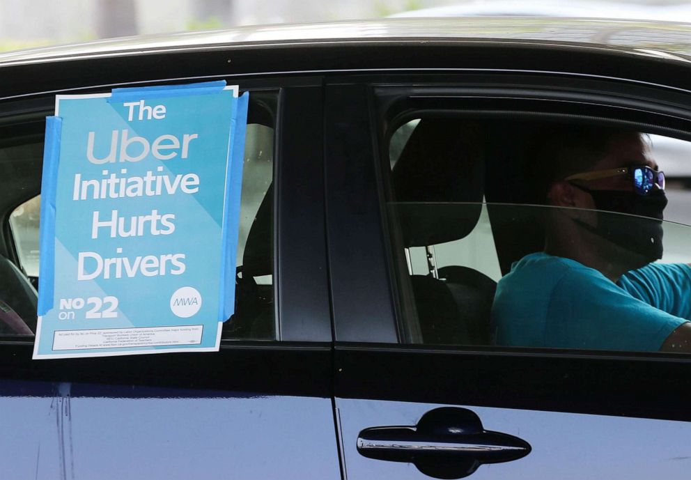 PHOTO: A ride-share driver displays a sign reading "The Uber Initiative Hurts Drivers" during a car rally by Uber and Lyft drivers calling for basic employment rights at Los Angeles International Airport on Aug. 20, 2020 in Los Angeles.