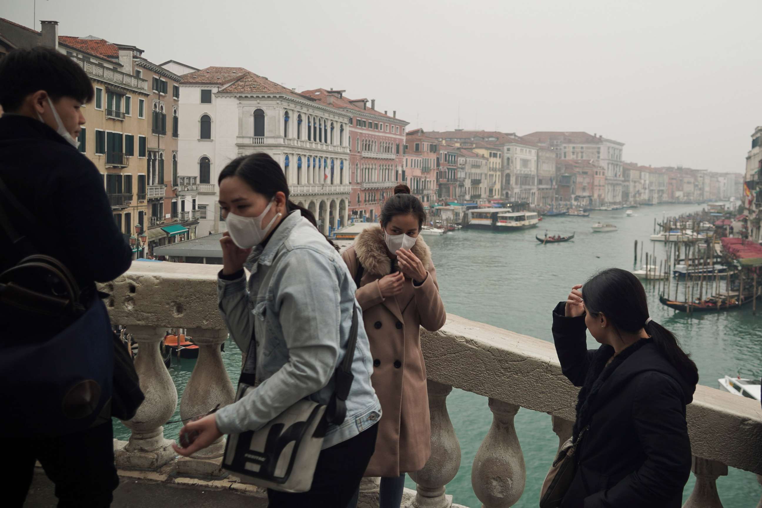 PHOTO: Tourists adjust their protective face masks as they take selfies atop Rialto bridge in Venice, Italy, Feb. 25, 2020.