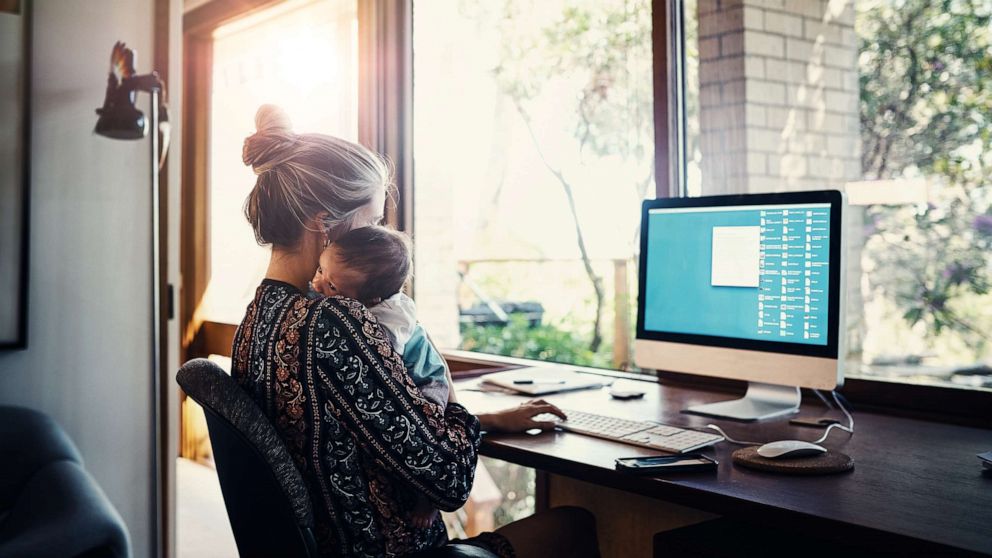PHOTO: A woman holds a child while using a computer in this stock photo.