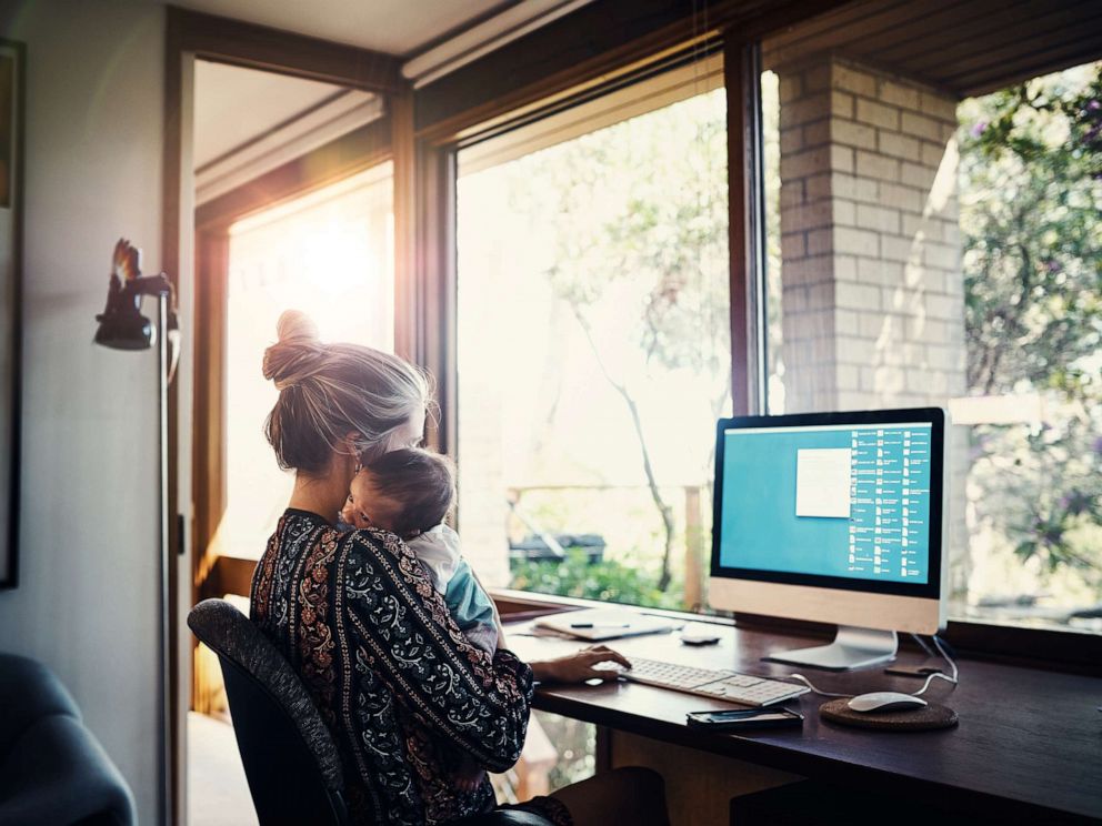 PHOTO: A woman holds a child while using a computer in this stock photo.