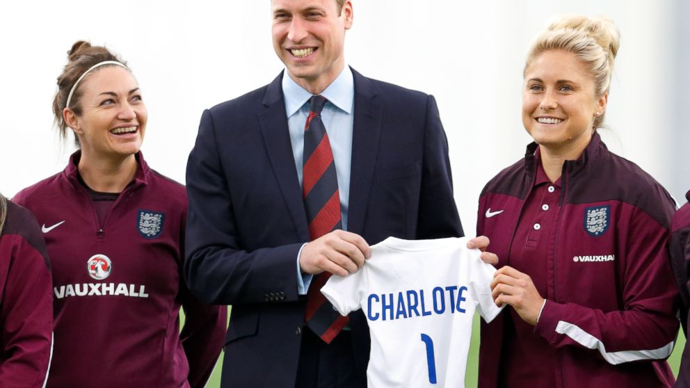 Prince William, Duke of Cambridge receives an England football shirt for daughter Princess Charlotte of Cambridge from Captain Steph Houghton, right, as he meets the England Women's Football Team at St George's Par,  May 20, 2015 in Burton-upon-Trent, England.