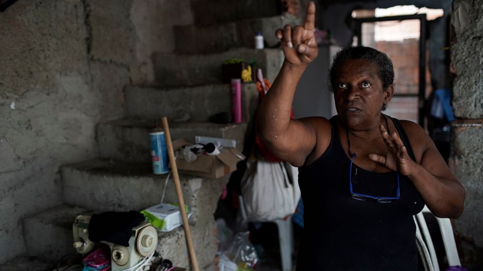 Vania Pereira da Silva, a seamstress and member of the Unidos de Padre Miguel samba school, points to a wall damaged by stray bullets inside her home in Rio de Janeiro, Brazil, Monday, Sept. 21, 2020. With the extra money scraped together sewing cost