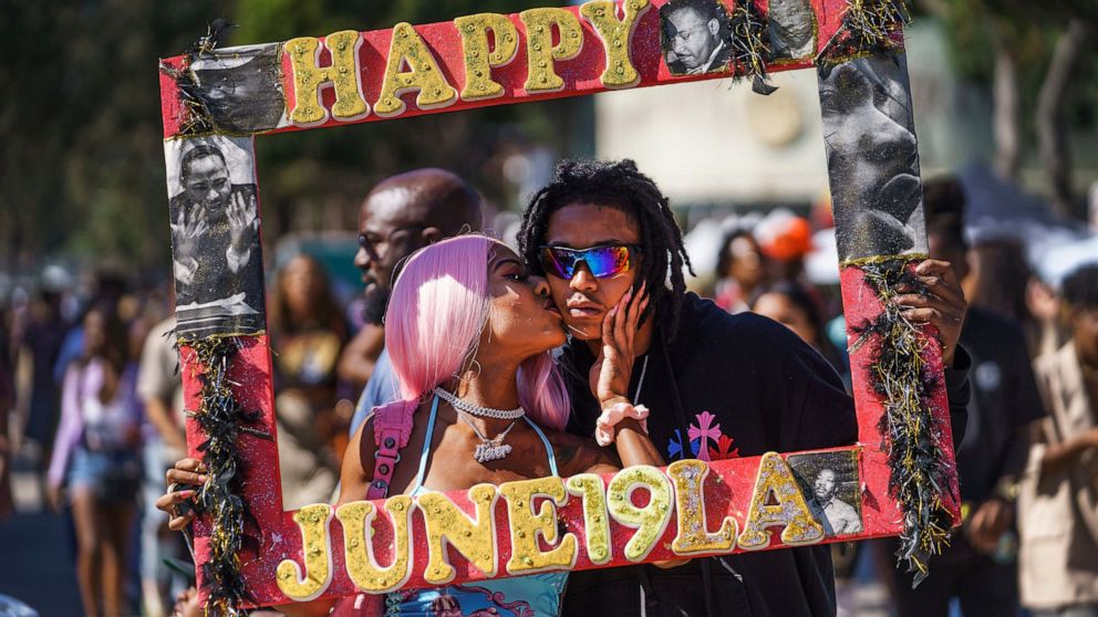 Daisa Chantel kisses Anthony Beltran as they take a picture to celebrate Juneteenth at Leimert Park in Los Angeles on Saturday, June 18, 2022. (AP Photo/Damian Dovarganes)