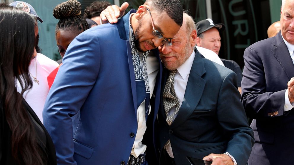 FILE — Grant Williams, left center, is embraced by his attorney Irving Cohen after his murder conviction is vacated, July 22, 2021, in New York. New York City has agreed to pay $7 million to Williams who spent 23 years behind bars for a murder he did