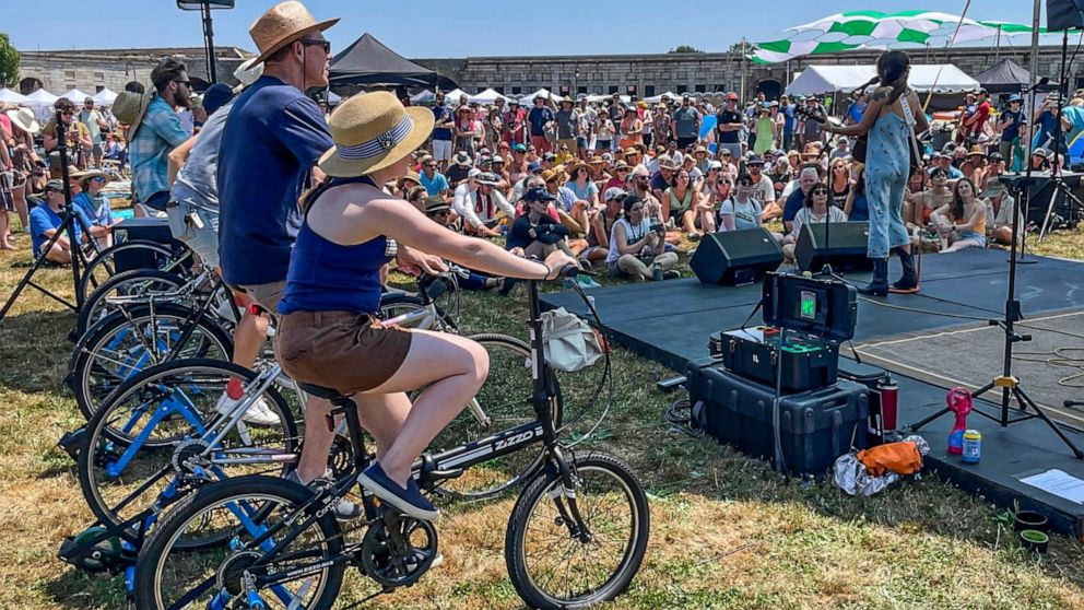 Madi Diaz, right, performs at the Newport Folk Festival's bike stage, powered in part by festivalgoers on stationary bicycles, left, Friday, July 22, 2022, in Newport, R.I. (AP Photo/Pat Eaton-Robb)