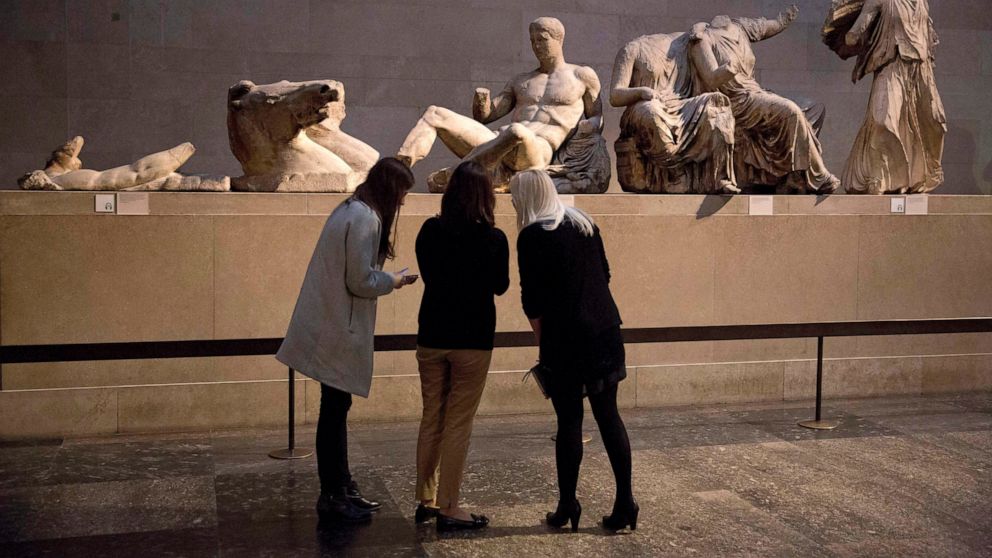 FILE - Women stand by a marble statue of a naked youth thought to represent Greek god Dionysos, center, from the east pediment of the Parthenon, on display during a media photo opportunity to promote a forthcoming exhibition on the human body in anci