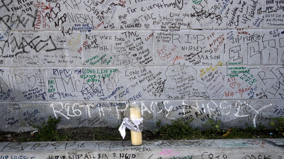 FILE - This April 11, 2019 file photo shows a lone candle against a wall full of messages commemorating slain rapper Nipsey Hussle outside The Marathon Clothing store in Los Angeles. Hussle, 33, was shot and killed outside his clothing store on March
