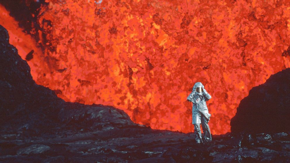 This image released by National Geographic shows Katia Krafft wearing an aluminized suit as she stands near lava burst at Krafla Volcano, Iceland, in a scene from the documentary "Fire of Love." (National Geographic via AP)