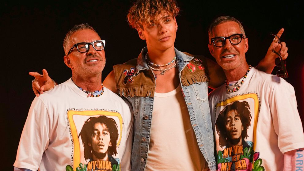 Designers Dean Caten, left, and Dan Caten, right, pose with a model backstage after the Dsquared2 men's Spring Summer 2023 collection presented in Milan, Italy, Friday, June 17, 2022. (AP Photo/Luca Bruno)
