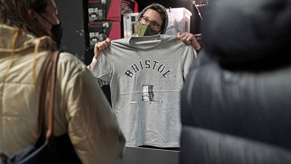 A person inside Rough Trade in Bristol, England, Saturday Dec. 11, 2021, holds up a T-shirt designed by street artist Banksy, being sold to support four people facing trial accused of criminal damage in relation to the toppling of a statue of slave t