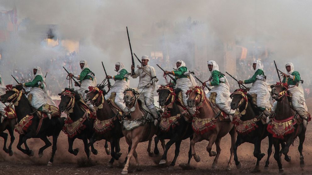 In this Thursday, July 25, 2019 photo, a troupe charges firing their rifles during Tabourida, a traditional horse riding show also known as Fantasia, in the coastal town of El Jadida, Morocco. Thousands of visitors descend on the Moroccan coastal cit