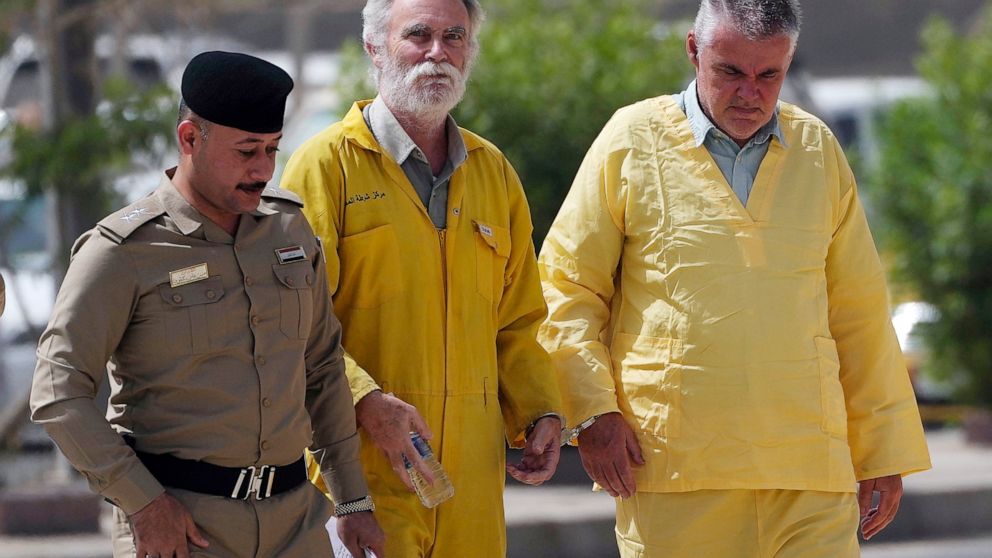 FILE - Volker Waldmann, right, and Jim Fitton, center, are handcuffed as they walk to a courtroom escorted by police arriving to court in Baghdad, Iraq, on May 22, 2022. A retired British geologist jailed in Iraq for antiquities smuggling has been fr
