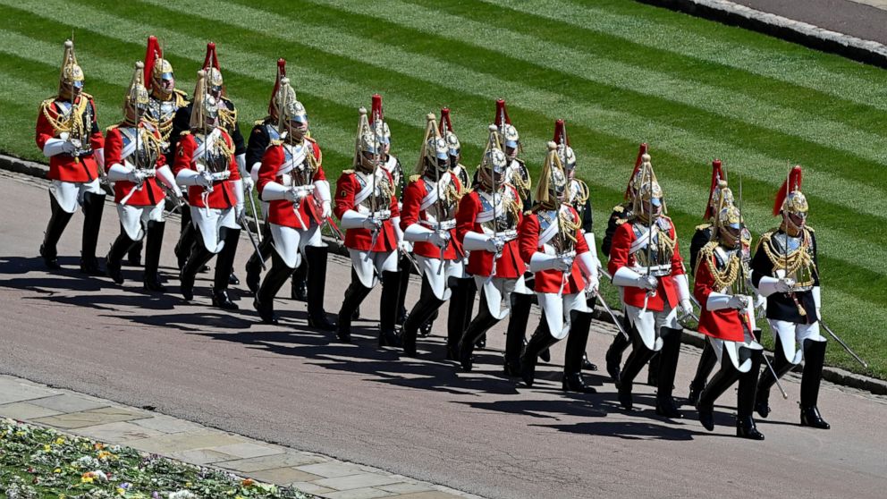 Military personnel in parade dress uniform march past flowers which where placed on the grass for the funeral of Britain's Prince Philip inside Windsor Castle in Windsor, England, Saturday, April 17, 2021. Prince Philip died April 9 at the age of 99 