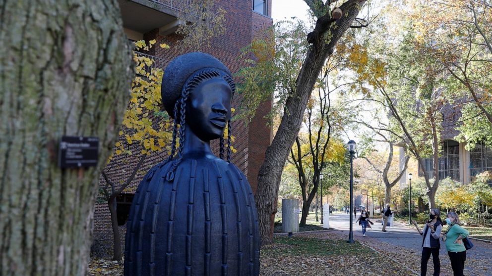 People look at a newly installed sculpture by artist Simone Leigh on the University campus in Philadelphia, Tuesday, Nov. 10, 2020. Leigh's 16-foot-tall bronze bust of a Black woman has been installed at the entrance to the heart of the University of