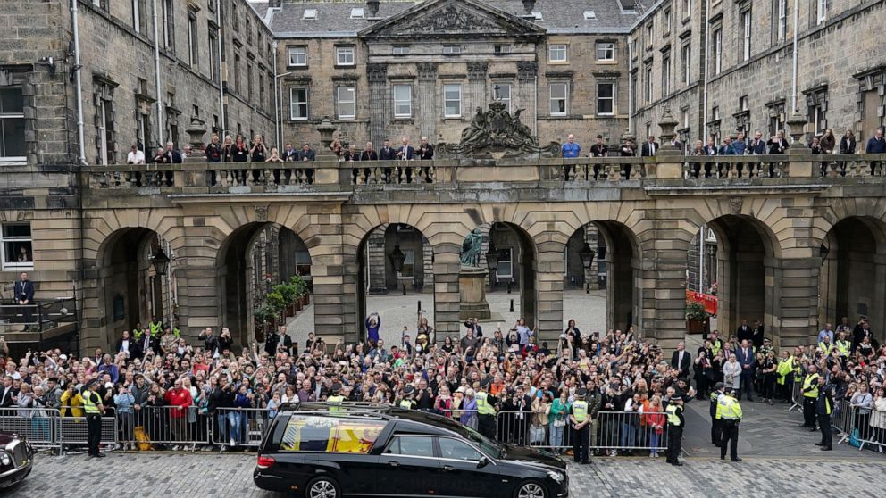 Crowds watch as the hearse carrying the coffin of Queen Elizabeth II, draped with the Royal Standard of Scotland, passes Mercat Cross in Edinburgh, Sunday, Sept. 11, 2022, as it continues its journey to the Palace of Holyroodhouse from Balmoral. (Ian