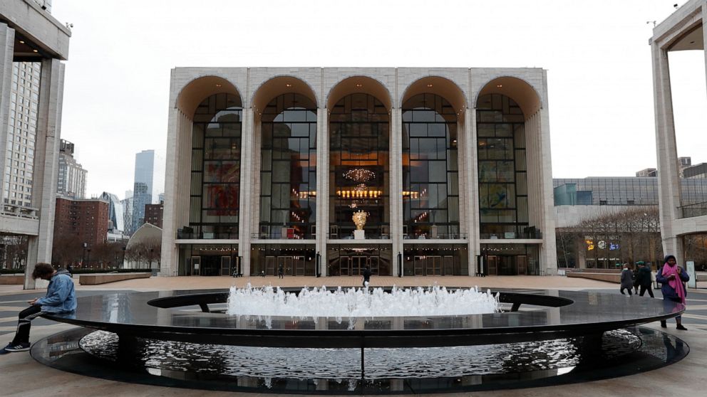 FILE - This March 12, 2020 file photo shows people by the fountain at Josie Robertson Plaza in front of The Metropolitan Opera house at Lincoln Center in New York. The Metropolitan Opera’s operating revenue dropped by $25 million to $150 million in t