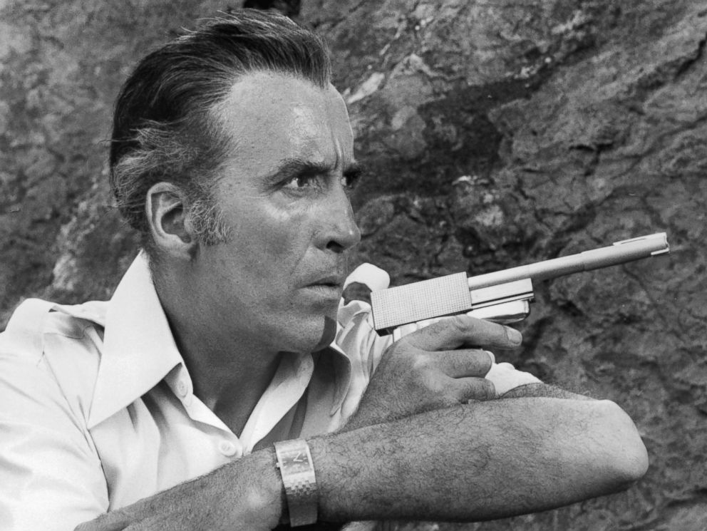 PHOTO: Christopher Lee along side a cliff wall pointing a gun in a scene from the film 'The Man With The Golden Gun', 1974.