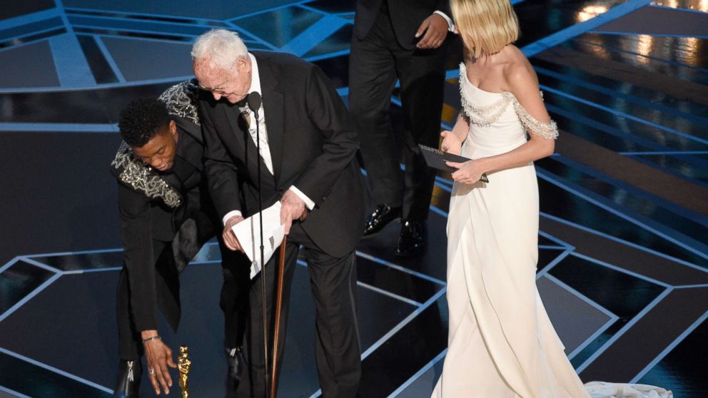 PHOTO: Chadwick Boseman, left, helps James Ivory, center, pick up his award for best adapted screenplay for "Call Me by Your Name" from the stage floor as Margot Robbie looks on at the Oscars, March 4, 2018, at the Dolby Theatre in Los Angeles.