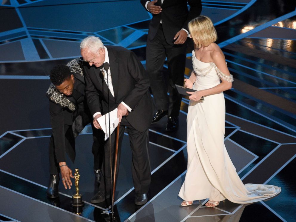 PHOTO: Chadwick Boseman, left, helps James Ivory, center, pick up his award for best adapted screenplay for "Call Me by Your Name" from the stage floor as Margot Robbie looks on at the Oscars, March 4, 2018, at the Dolby Theatre in Los Angeles.