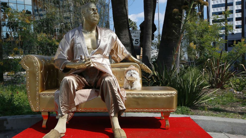 PHOTO: A dog poses next to a golden statue of a bathrobe-clad Harvey Weinstein, seated atop a couch on the sidewalk along Hollywood Blvd., in Los Angeles, March 1, 2018.