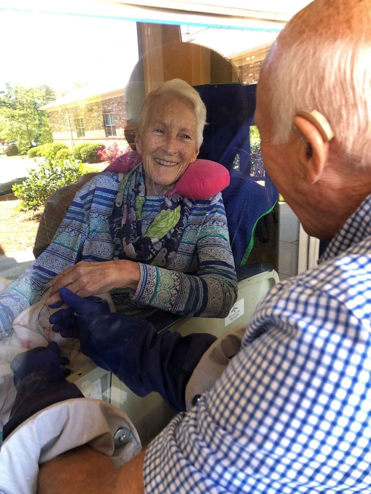 PHOTO: Jan Glass and George Glass hold hands through their daughter Cindy’s “Safe Hug Window” creation.