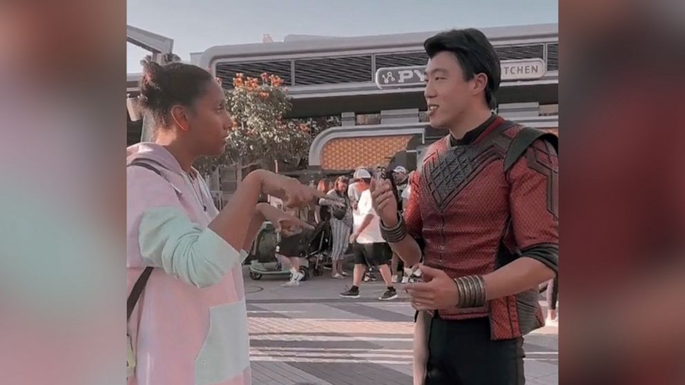 Shang-Chi character uses sign language with a guest at Avengers Campus.