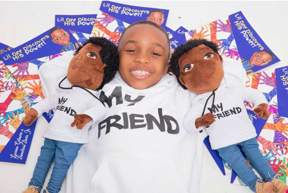 PHOTO: Demetrius sits with two My Friend dolls and several copies of his book. 