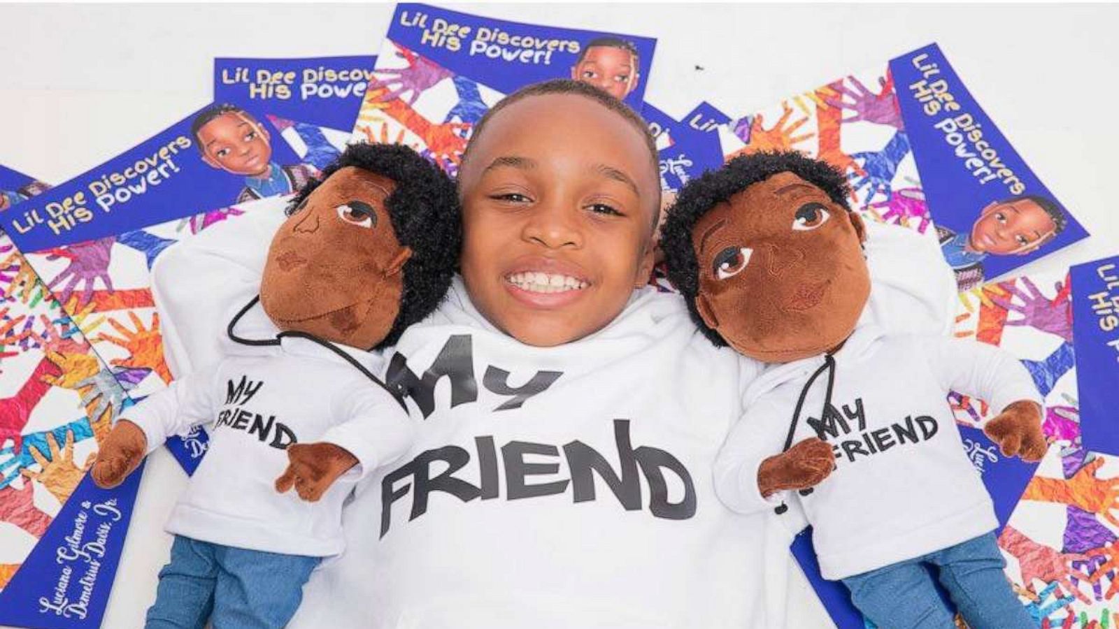 PHOTO: Demetrius sits with two My Friend dolls and several copies of his book.