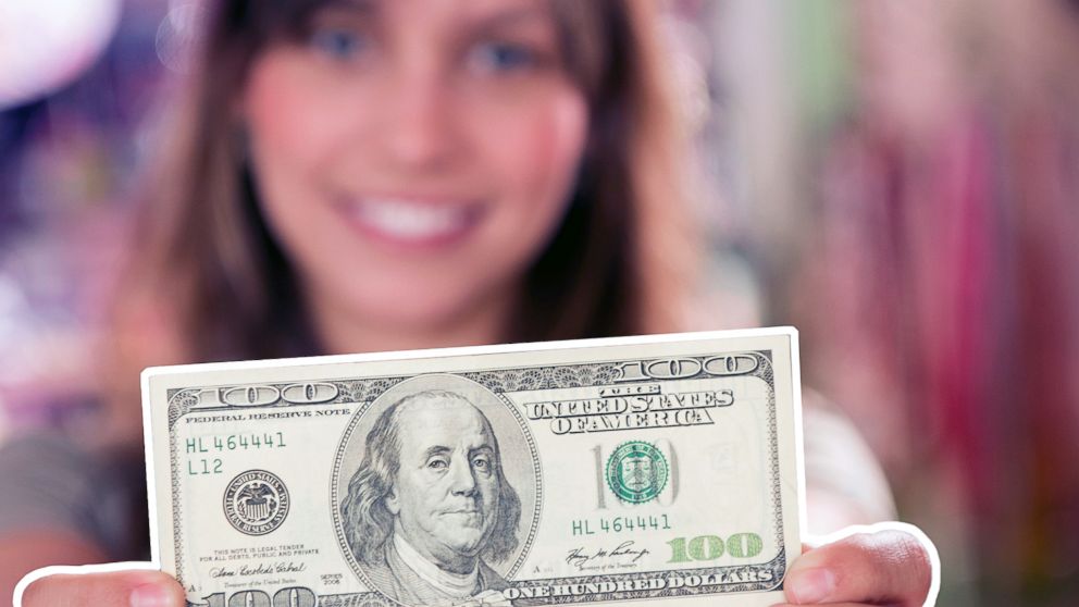 A woman holds a $100 bill in an undated stock photo.
