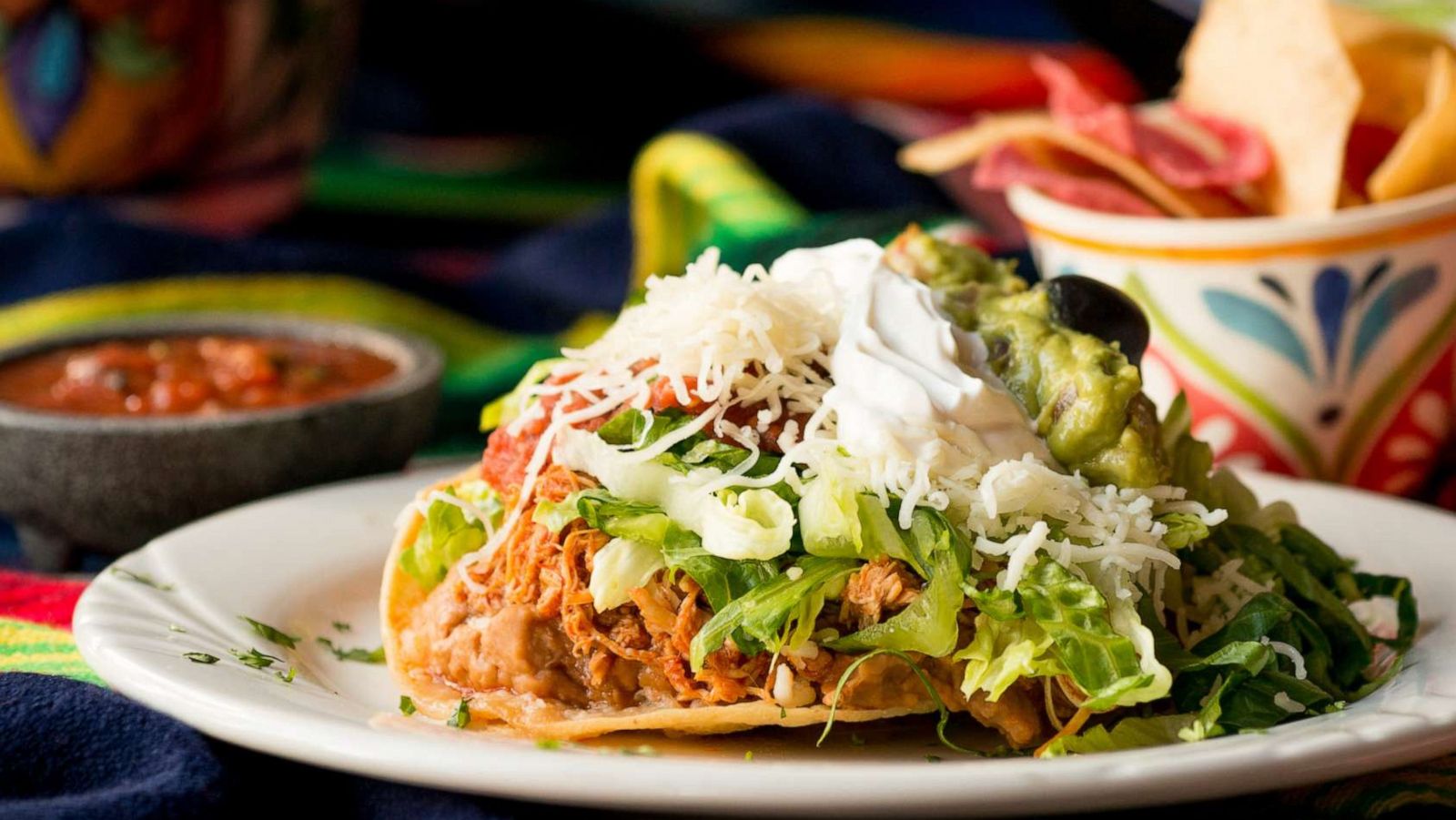 PHOTO: Crispy tortilla tostada with chicken, beans, lettuce, cheese, guacamole, sour cream, and salsa. Served with chips and dipping salsa styled on a sarape.