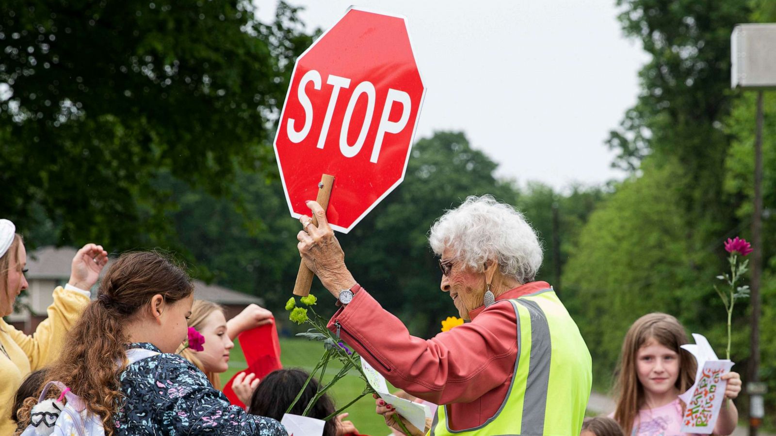 PHOTO: Students greet crossing guard Sandra Bellew with hugs, handwritten signs and flowers on May 19, 2023, ahead of her retirement.